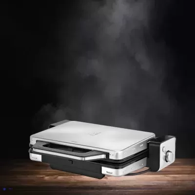 Chapa elétrica prata e preta sobre madeira com vapor no fundo preto