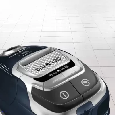 Aspirador de pó azul e prata com botões e texto Aquarus Silence System sobre chão azulejado