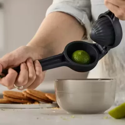 Espremedor de limão preto com limão dentro e tigela cinza em fundo de cozinha