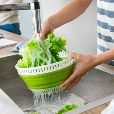 Pessoa a lavar alface em escorredor verde e branco na pia