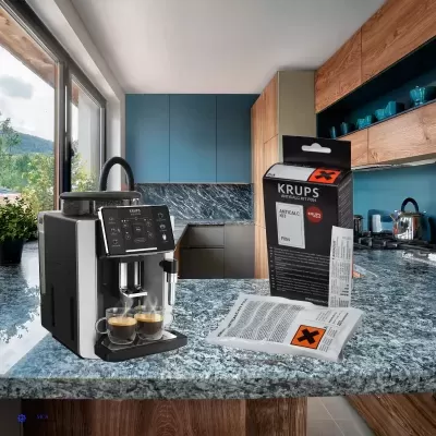 Máquina de café Krups em inox e preto numa cozinha moderna com armários azuis e madeira, com caixa e saco Anticalc Krups em bancada azul marmoreada.