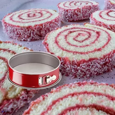 Forma de tarte redonda de mola vermelha ao lado de fatias de bolo espiral branco e vermelho com coco ralado