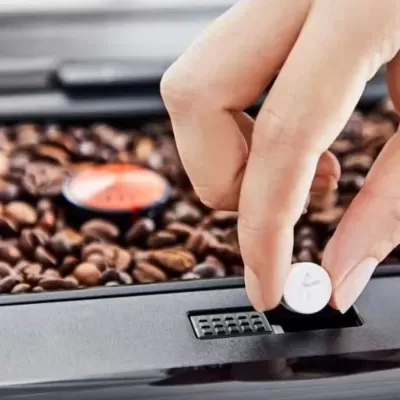 Mão segurando comprimido branco sobre máquina preta com grãos de café