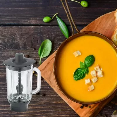 Tigela de sopa laranja com croutons e manjericão e liquidificador com copo transparente
