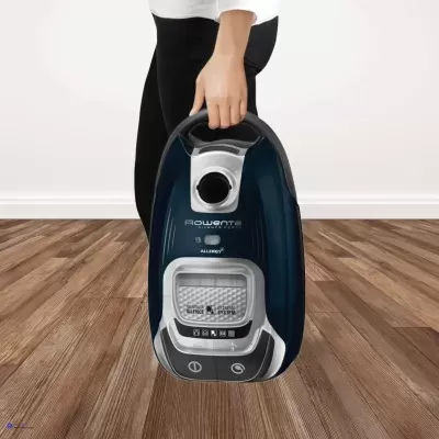 Aspirador Rowenta azul escuro e cinza segurado por pessoa com roupa preta e branca no chão de madeira