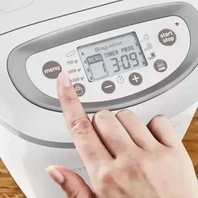 Painel digital de máquina de pão branca com botões e display, mão a tocar no botão menu