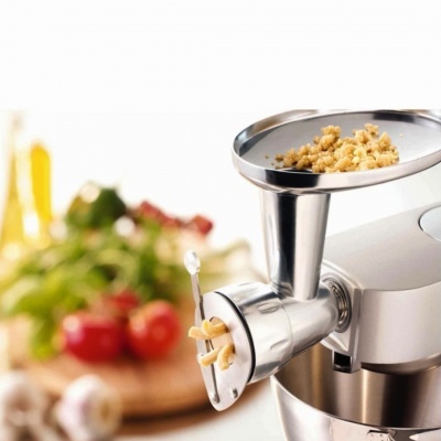 Moedor elétrico de carne com massa de salsicha e legumes ao fundo