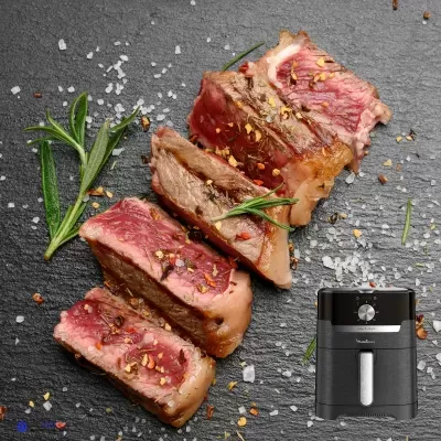 Pedaços de carne grelhada com temperos sobre ardósia ao lado de fritadeira preta