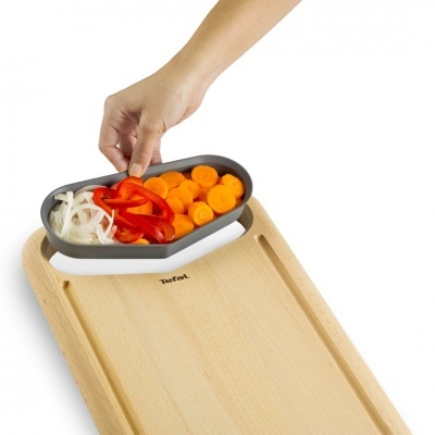 tábua de madeira com colher plástica a conter legumes cortados e mão a segurar