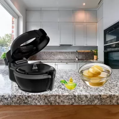 Máquina de pão preta aberta em bancada de granito com tigela de batatas e frasco de azeite numa cozinha moderna