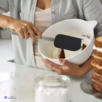 Pessoa a usar espátula preta e taça branca com creme e pó castanho numa bancada