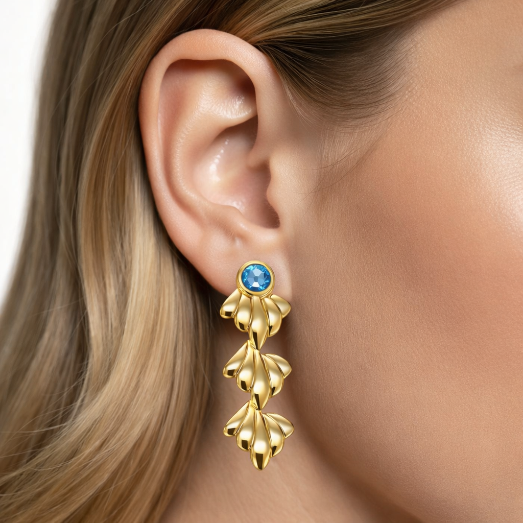 Brinco dourado pendente com pedra azul na orelha de uma pessoa.