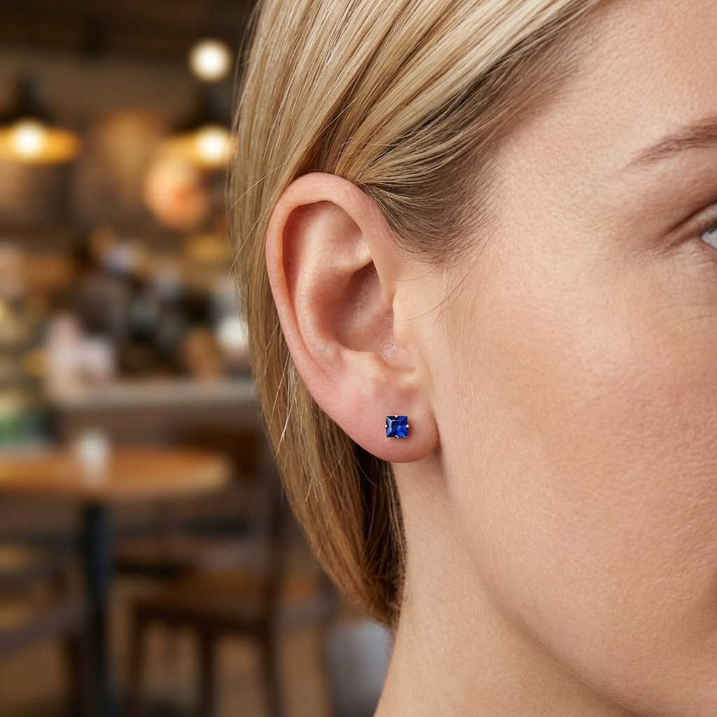 Brinco quadrado azul escuro em orelha feminina com interior de café desfocado ao fundo