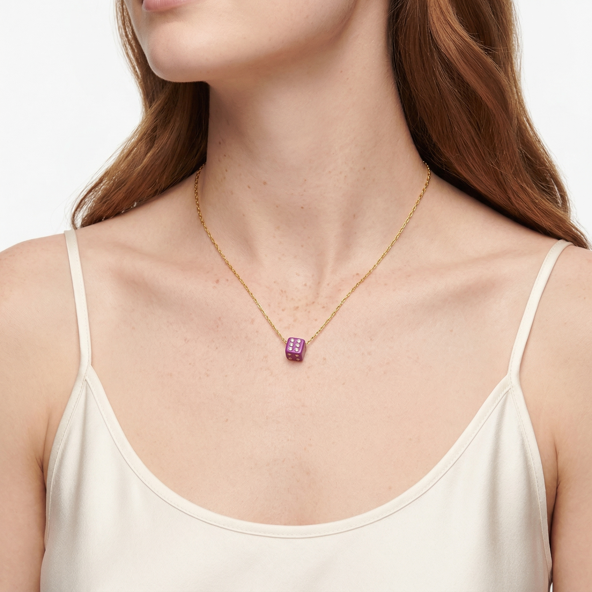 Colar dourado com pendente dado roxo em pescoço de mulher com vestido creme