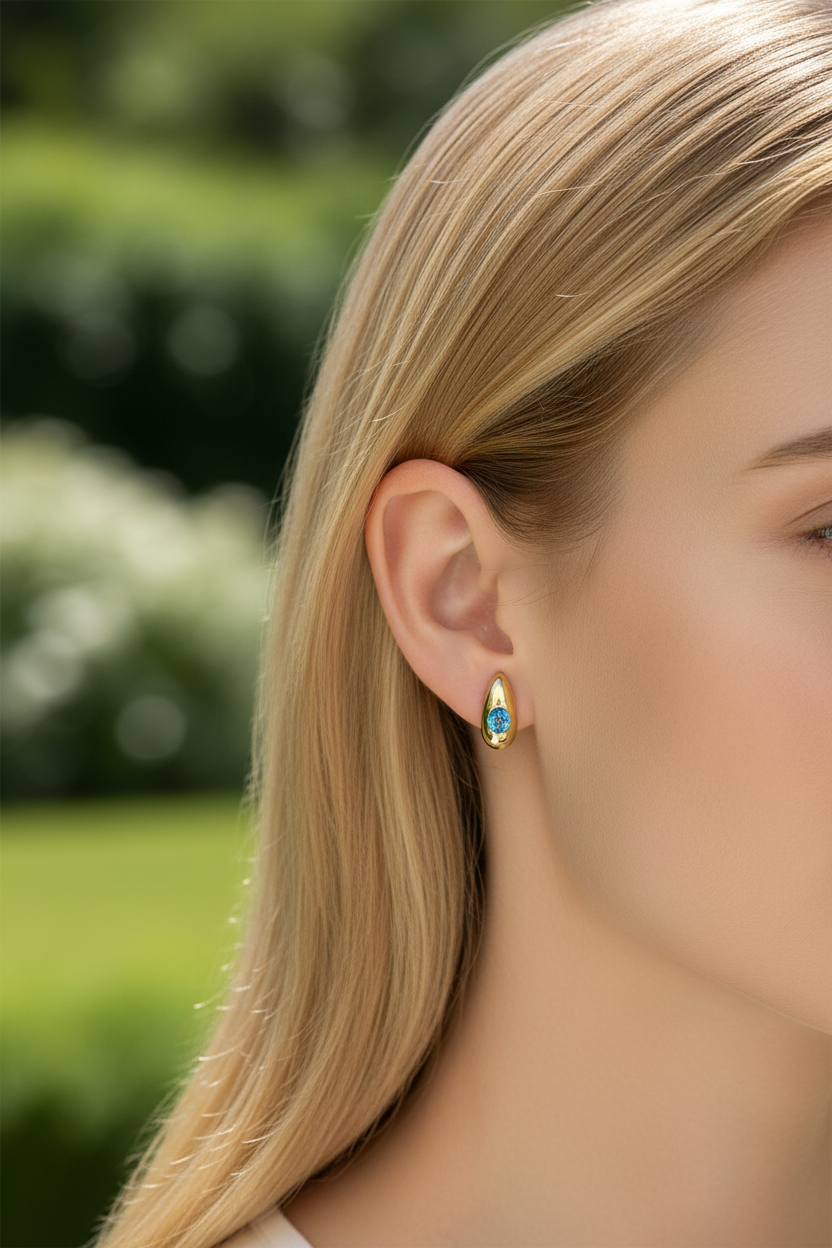 Brinco dourado em forma de gota com pedra azul no centro na orelha de uma mulher