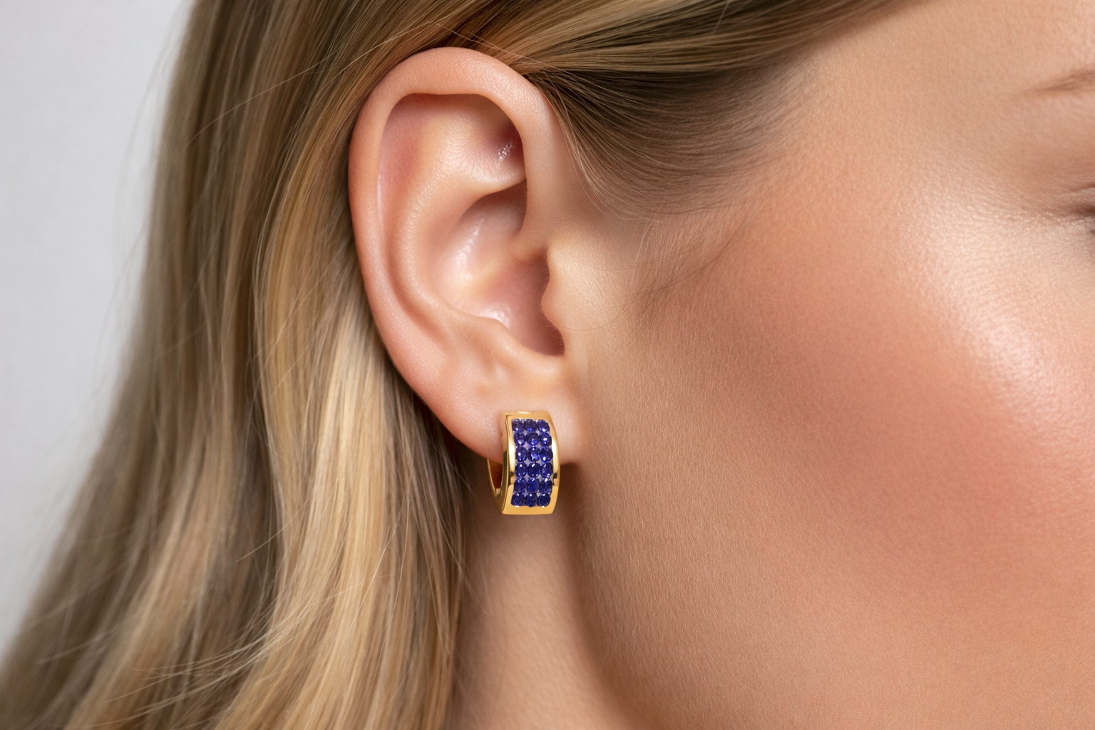 Brinco dourado com pedras azuis usado na orelha