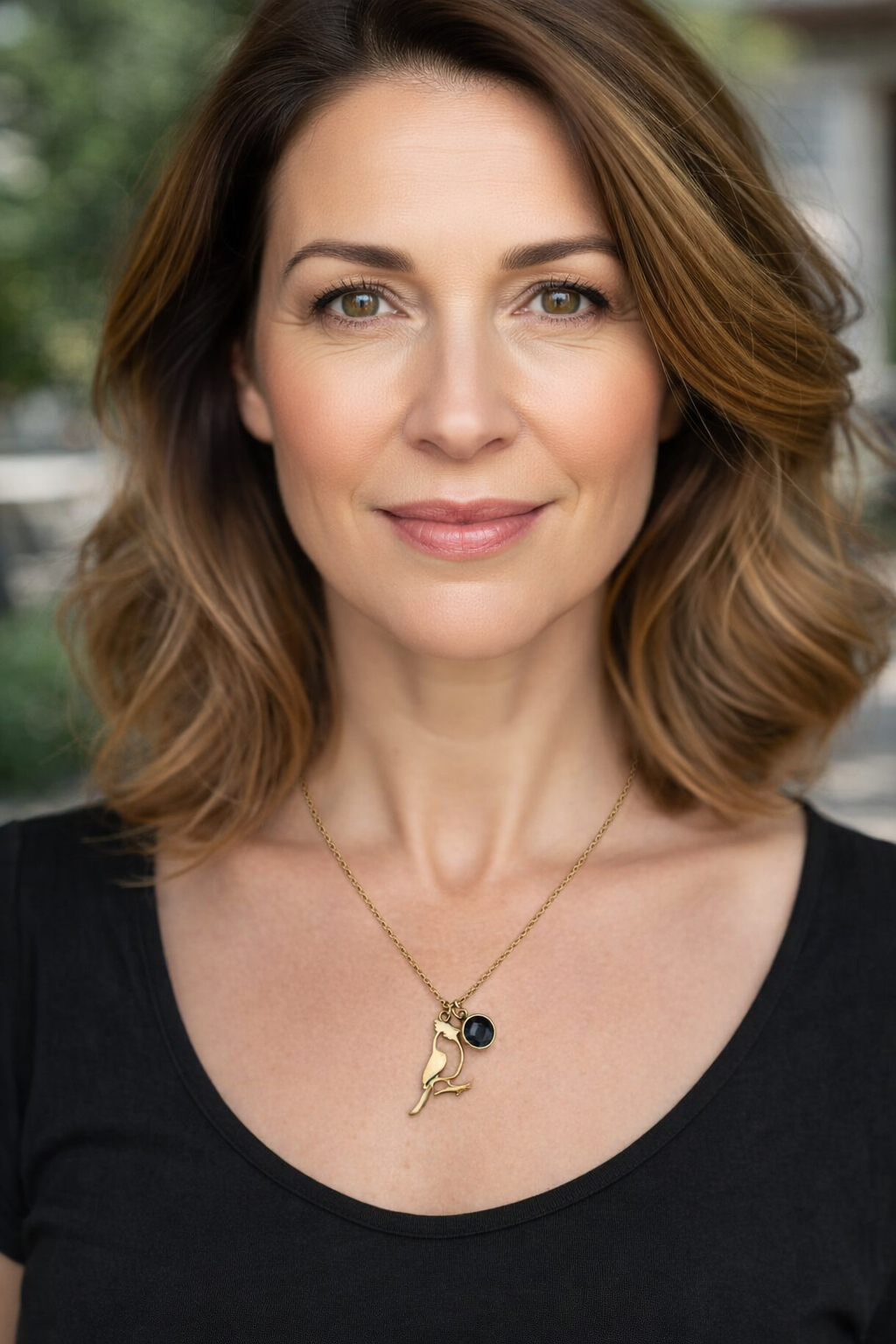 Colar dourado com pendente de pássaro e pedra preta em mulher com t-shirt preta