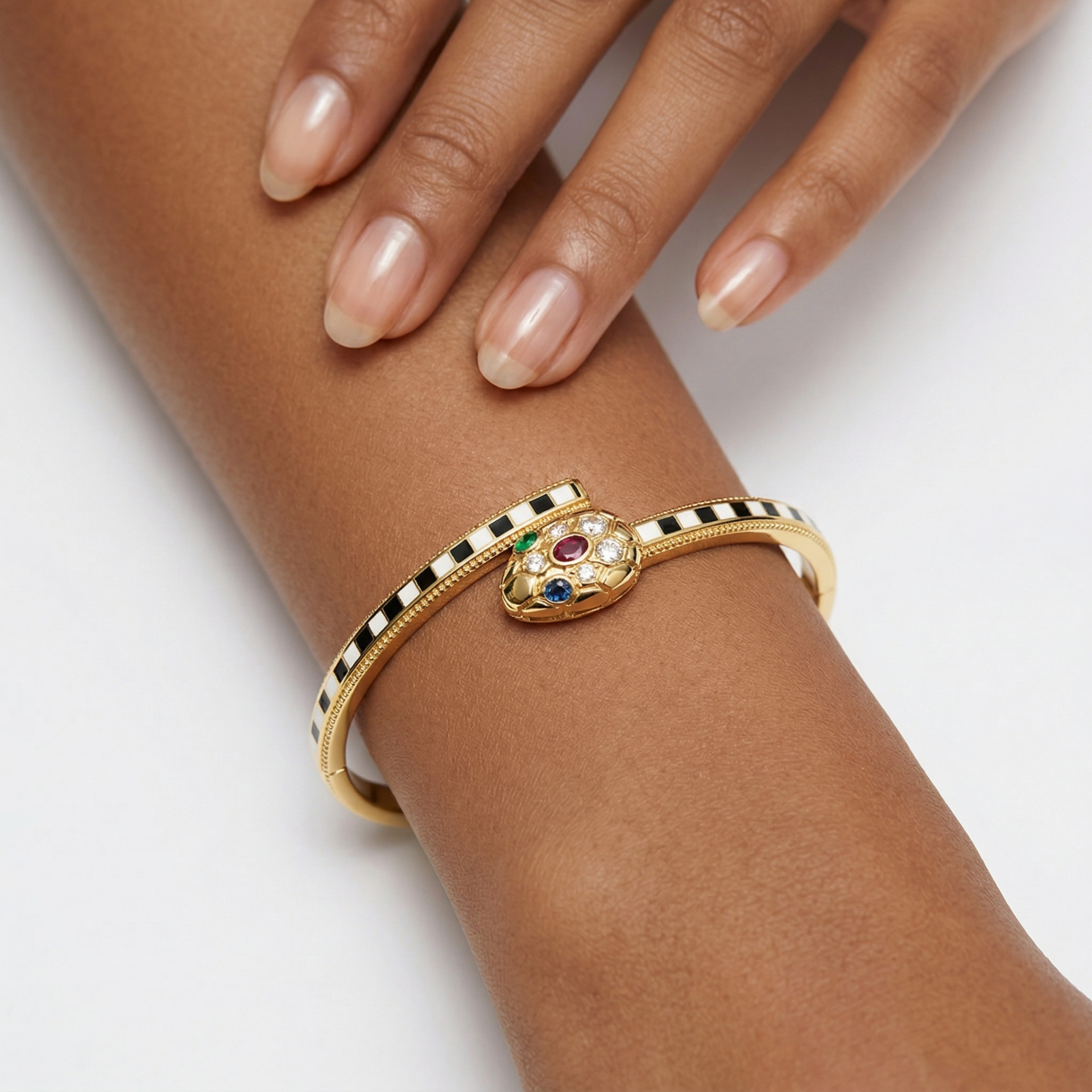 Pulseira dourada com padrão xadrez e cabeça de cobra com pedras preciosas.