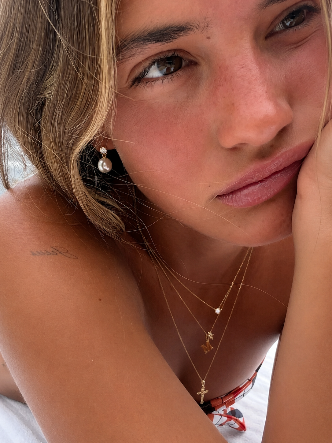 Colar dourado com pendentes e brinco com pérola em modelo bronzeado
