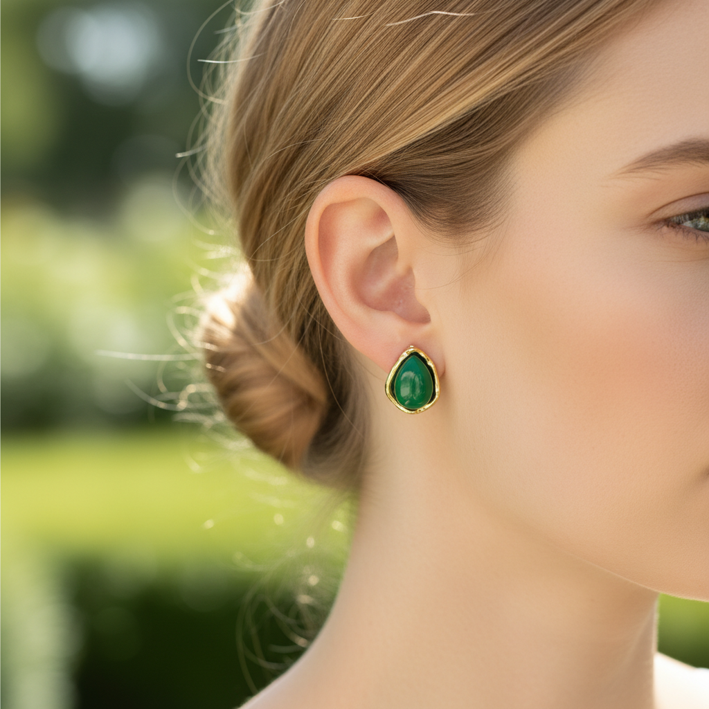 Brinco de botão com pedra verde e moldura dourada no ouvido de mulher.