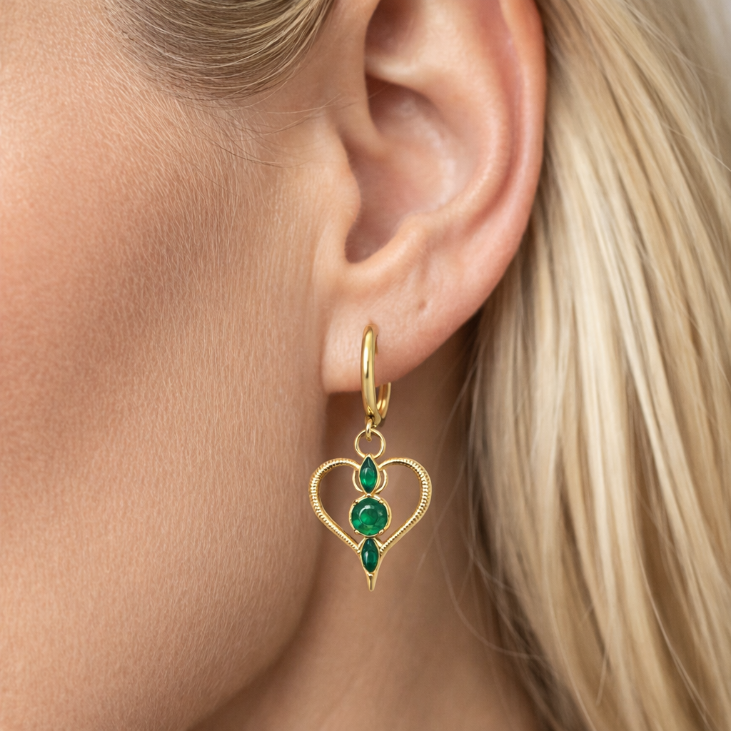 Brinco dourado com pedras verdes em forma de coração na orelha de uma pessoa