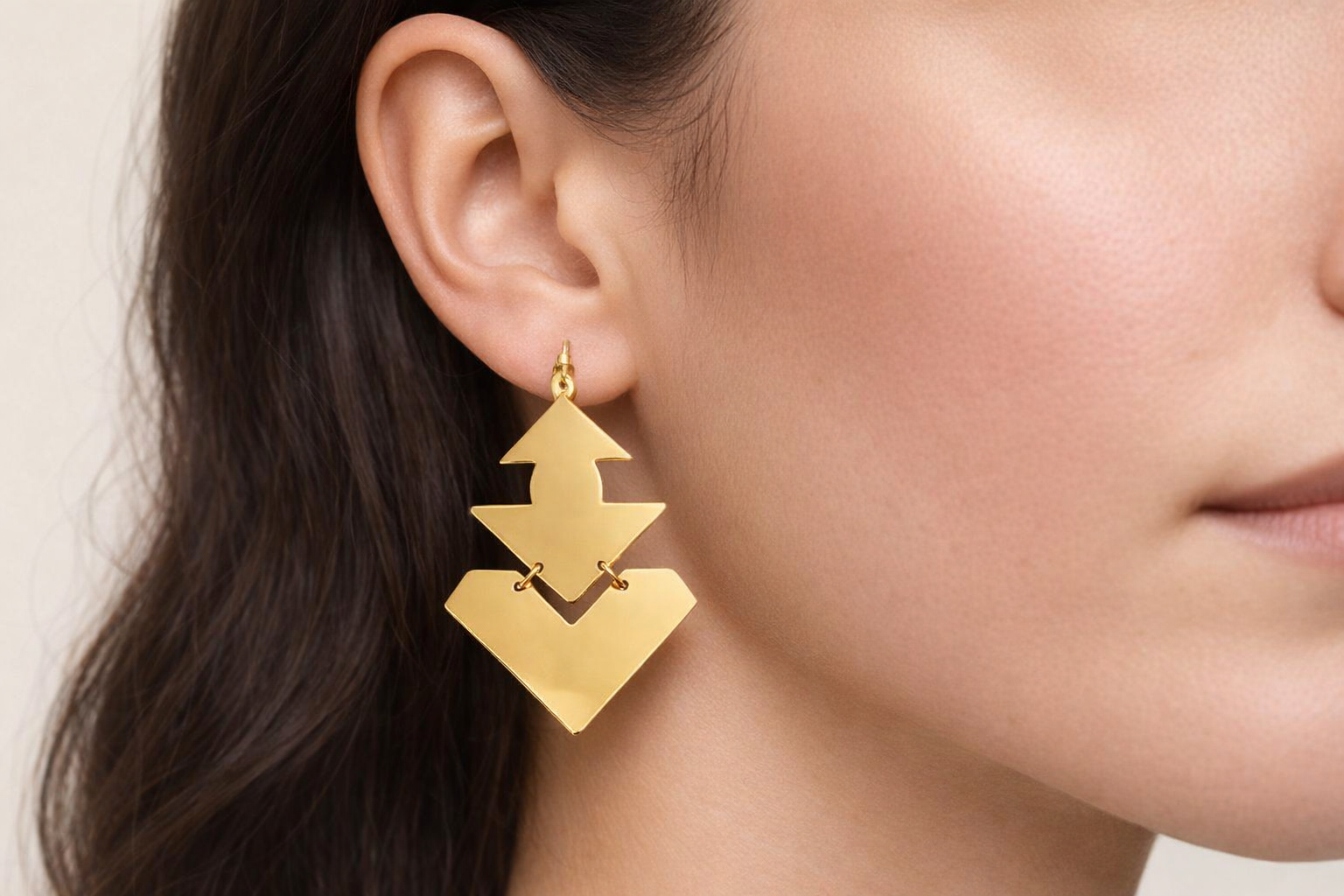 Brinco dourado geométrico com triângulos e quadrados numa orelha feminina