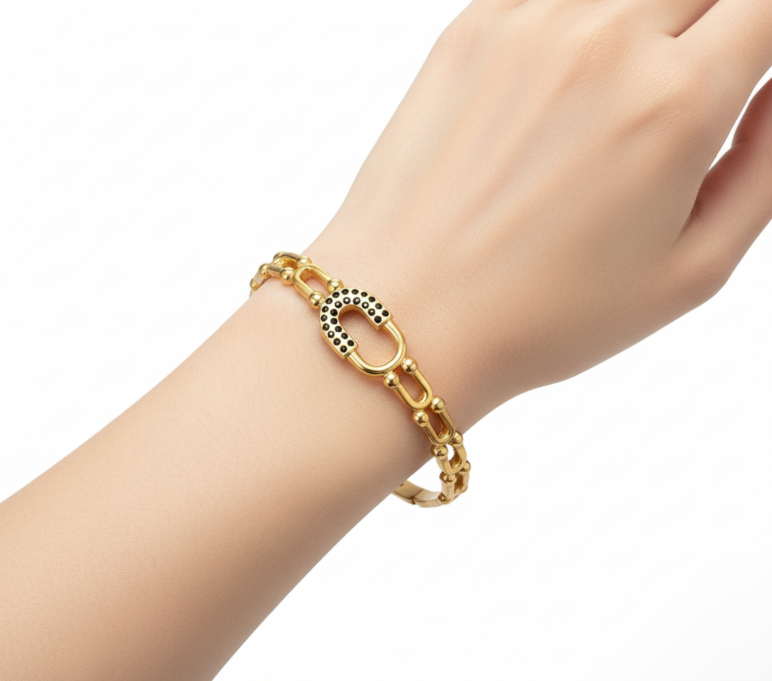 Pulseira dourada com elos e detalhe oval com pontos pretos num pulso