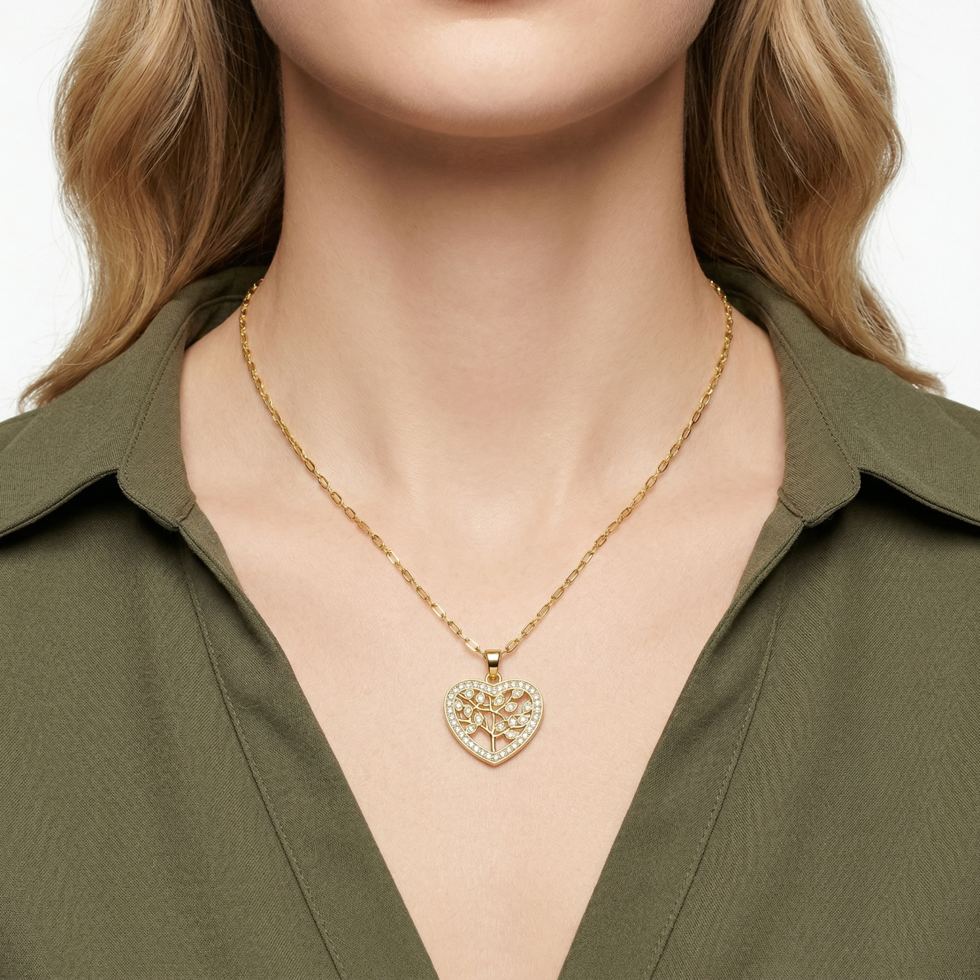 Colar dourado com pendente em forma de coração e árvore, usado por modelo com camisa verde.
