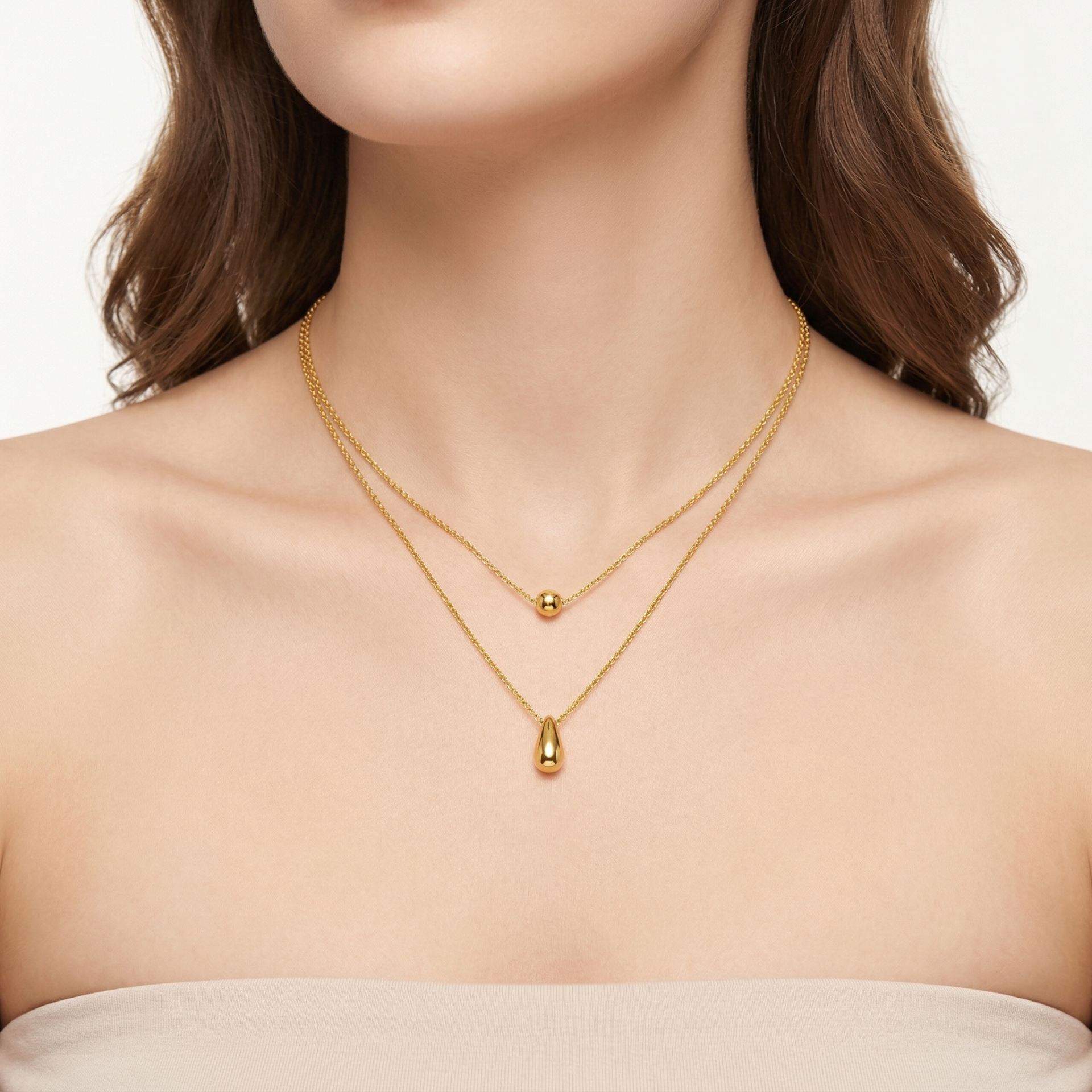 Colar duplo dourado com pendentes redondo e em gota num pescoço feminino