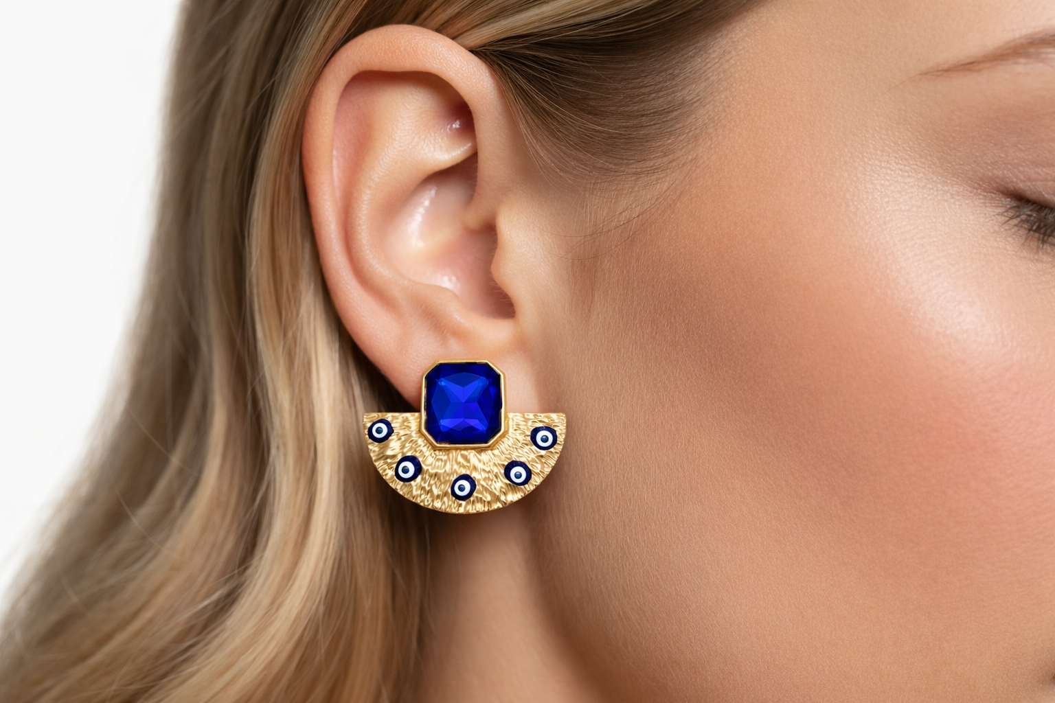 Brinco dourado texturizado com pedra azul quadrada e detalhes em círculos azuis e brancos.