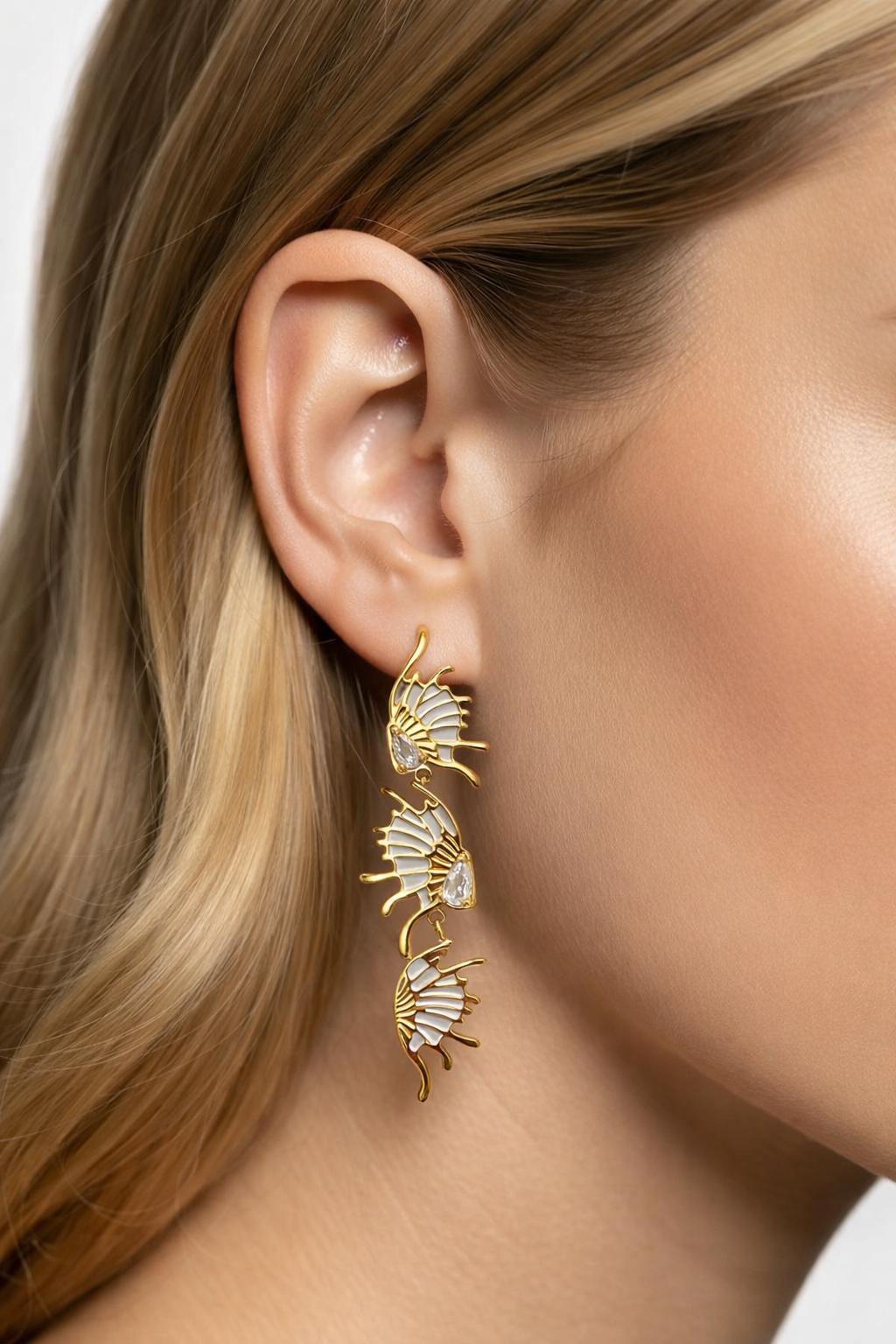 Brinco pendente dourado com três conchas e pedras transparentes numa orelha feminina