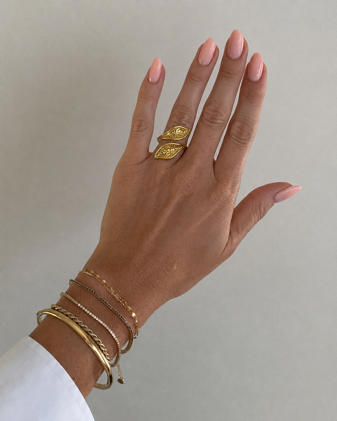 Mão com anel duplo dourado e pulseiras finas em fundo claro