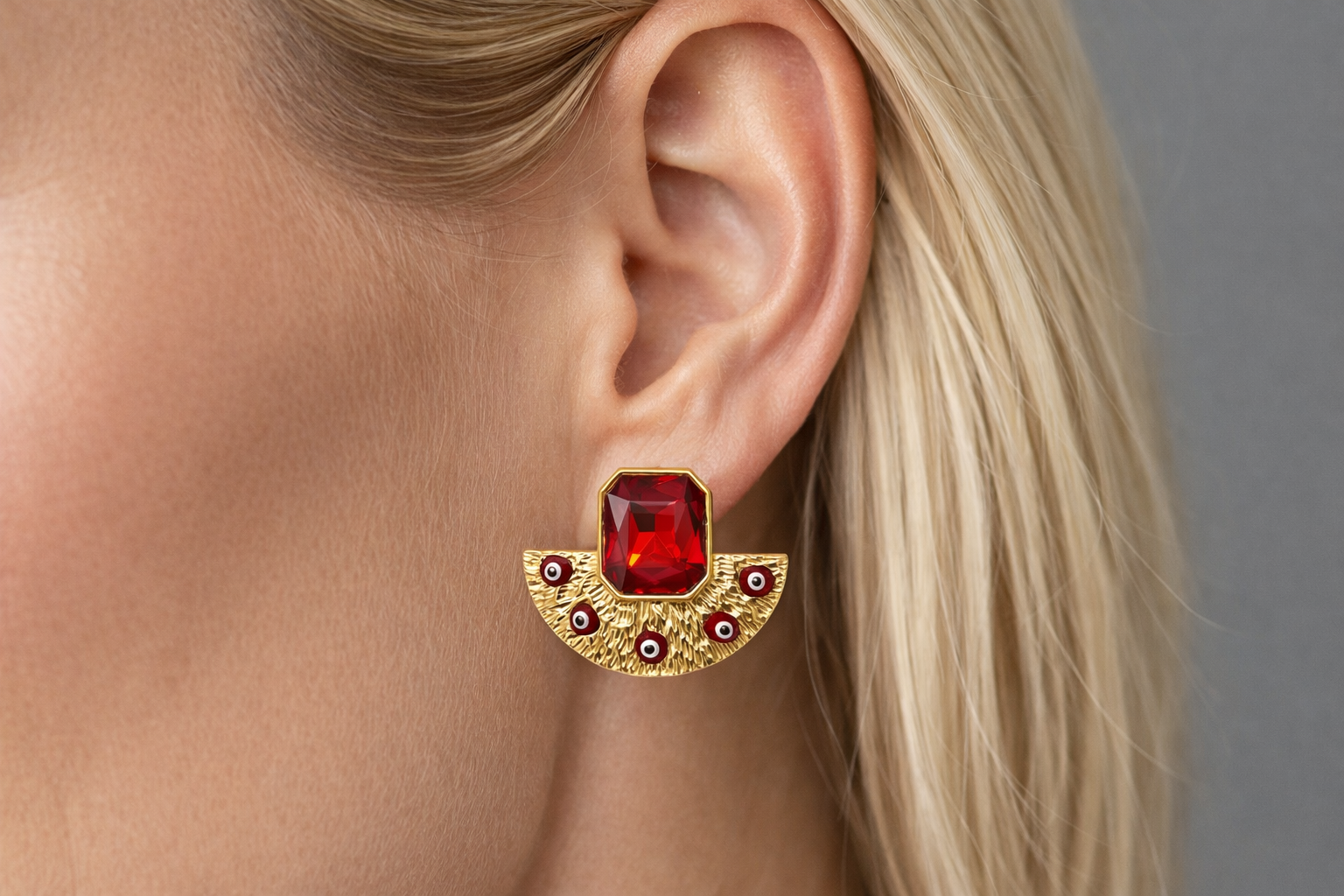Brinco dourado com pedra vermelha retangular no centro em orelha de mulher