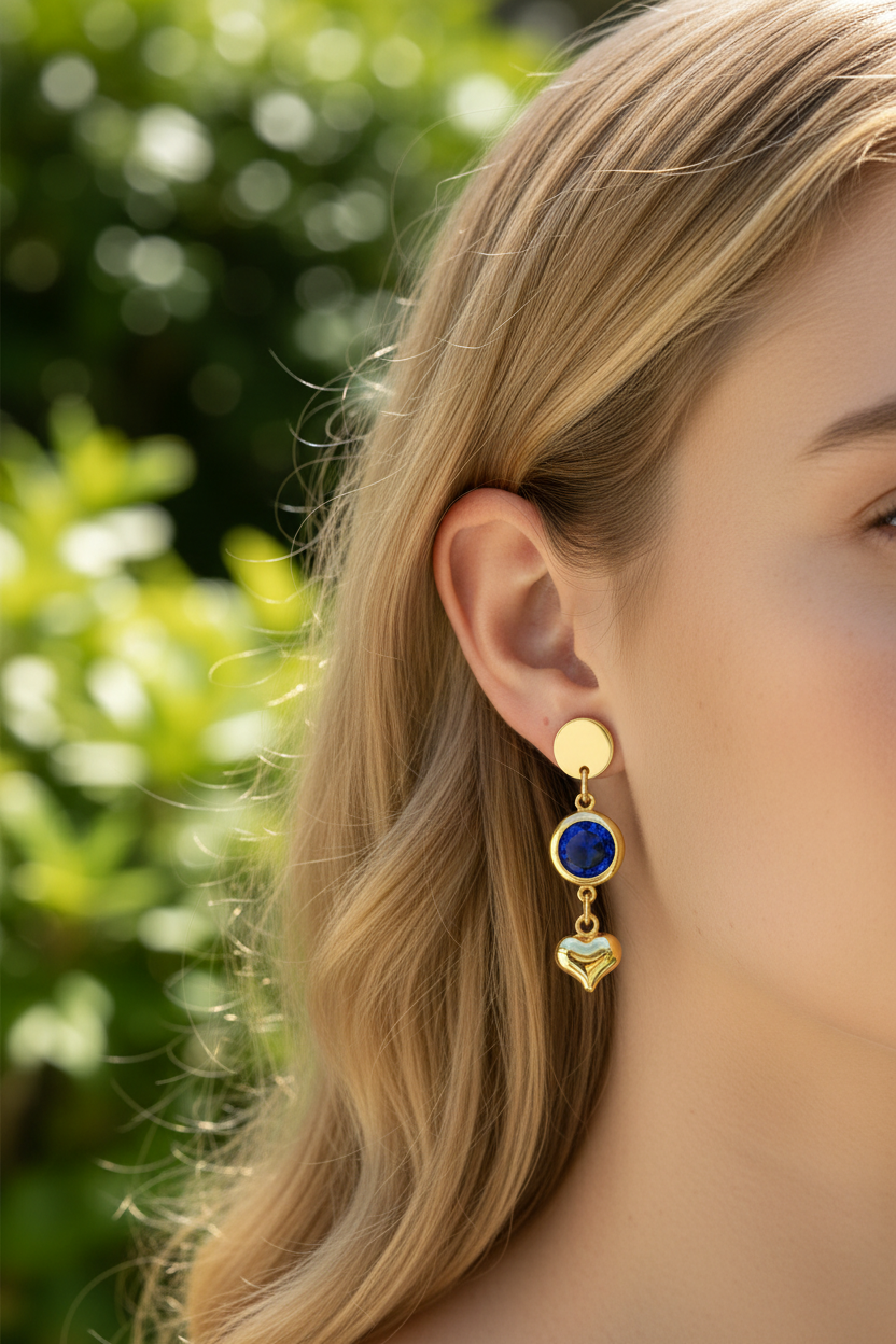 Brinco pendente dourado com pedra azul e coração dourado junto à orelha feminina.