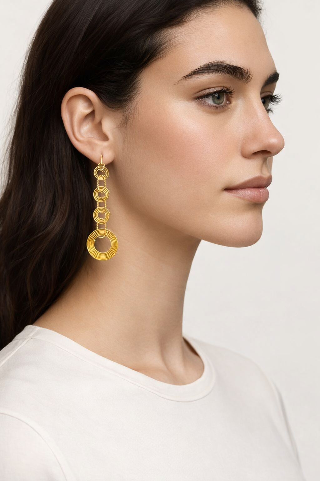 Brincos dourados em sequência de anéis concêntricos em modelo com t-shirt branca