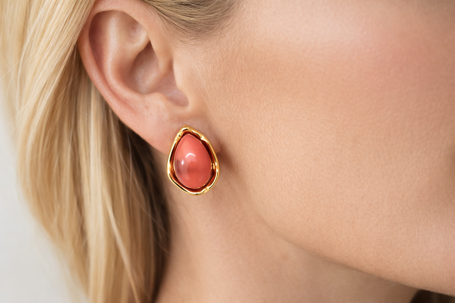 Brinco em forma de gota com pedra coral e borda dourada na orelha