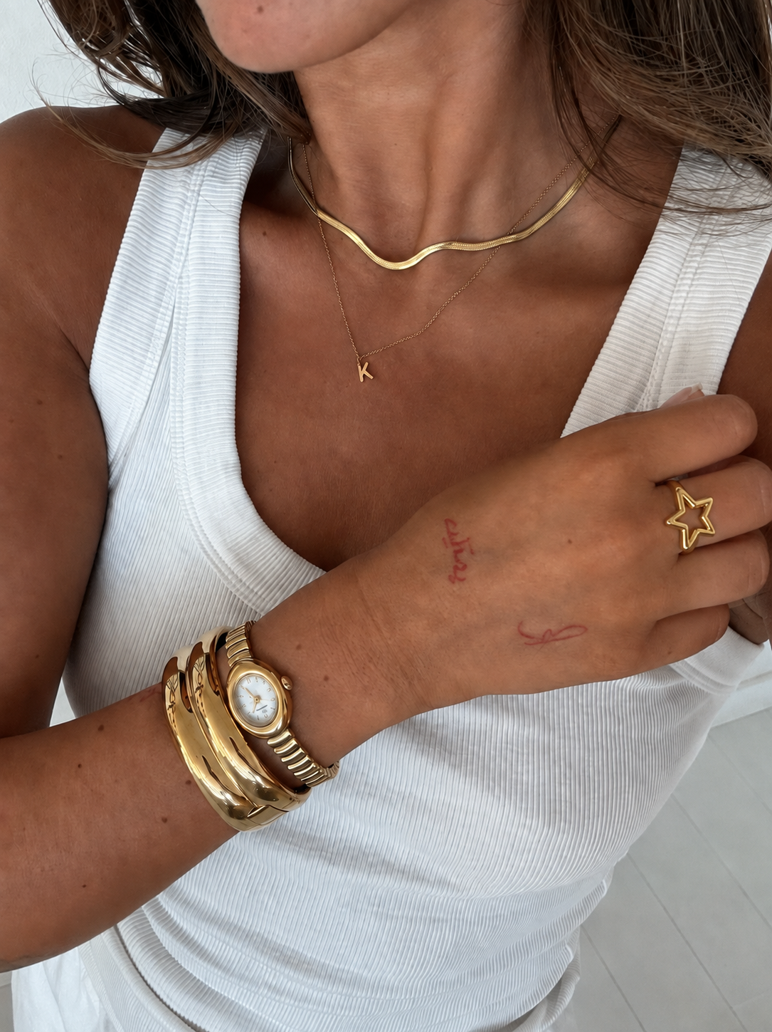 Mulher com pulseira dourada, relógio, colares e argola em forma de estrela em camisola branca