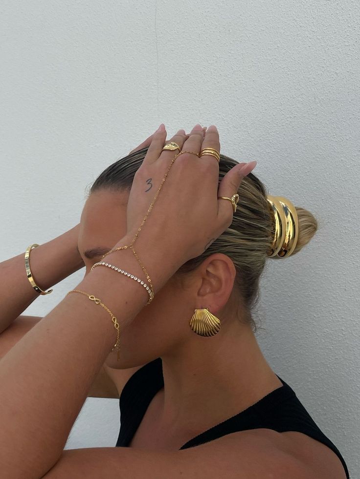 Mulher com acessórios dourados e cabelo preso em coque, fundo branco