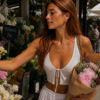 Mulher ruiva com top branco e saia, segurando flores rosadas em mercado
