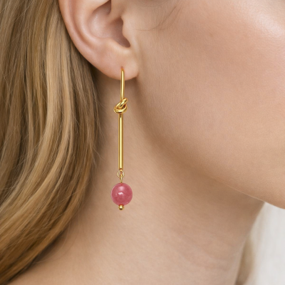 Brinco dourado com esfera rosa pendente numa orelha feminina