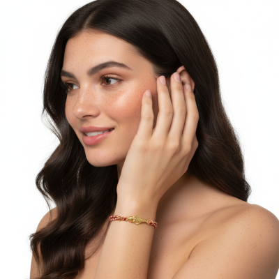 Pulseira dourada com peça de peixe e corda vermelha no pulso de mulher com cabelo castanho