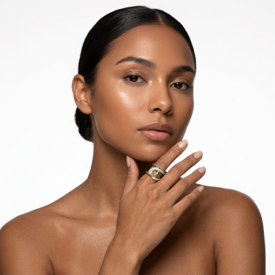 Mulher morena com anel dourado e verde claro na mão junto ao rosto