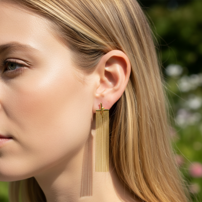 Brincos dourados compridos em mulher loira com fundo verde desfocado.