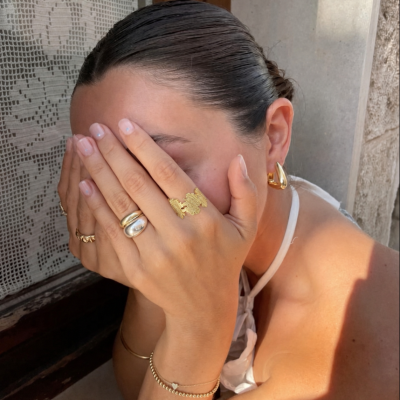 Mulher com anéis e pulseira dourados a esconder o rosto com as mãos