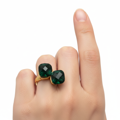 Anel dourado com pedras verdes facetadas no dedo médio de uma mão