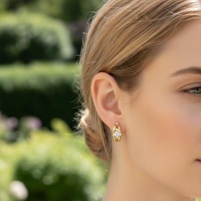 Brincos dourados de argola com pedra brilhante central em mulher com cabelo preso ao ar livre.