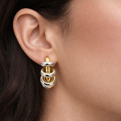 Brincos redondos em dourado e prateado na orelha de mulher.