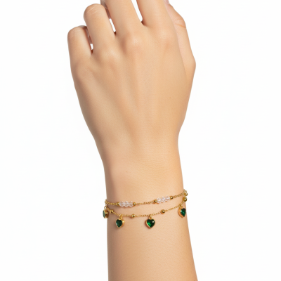 Pulseira dourada com pingentes em forma de coração verde no pulso