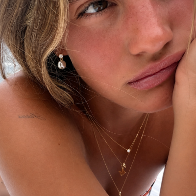 Colar dourado com pendentes e brinco com pérola em modelo bronzeado