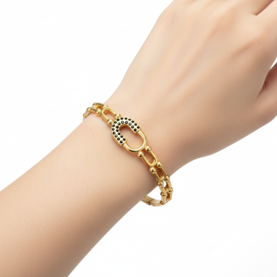 Pulseira dourada com elos e detalhe oval com pontos pretos num pulso